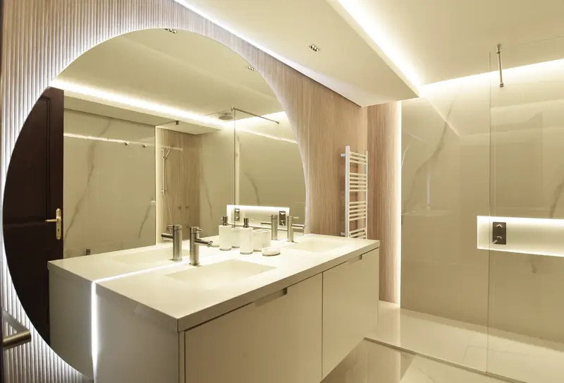 Baño de mármol blanco con espejo en arco, doble lavabo y ducha de cristal con un nicho iluminado