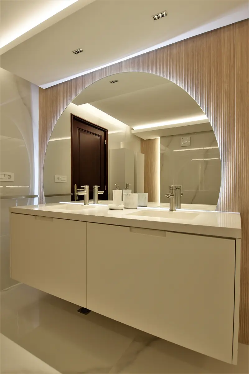 Baño con un gran espejo en arco sobre listones de madera, doble lavabo blanco y luz en el techo