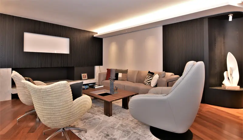 Estar con paredes de listones de madera oscura, sillones tejidos, sillón gris y una escultura blanca