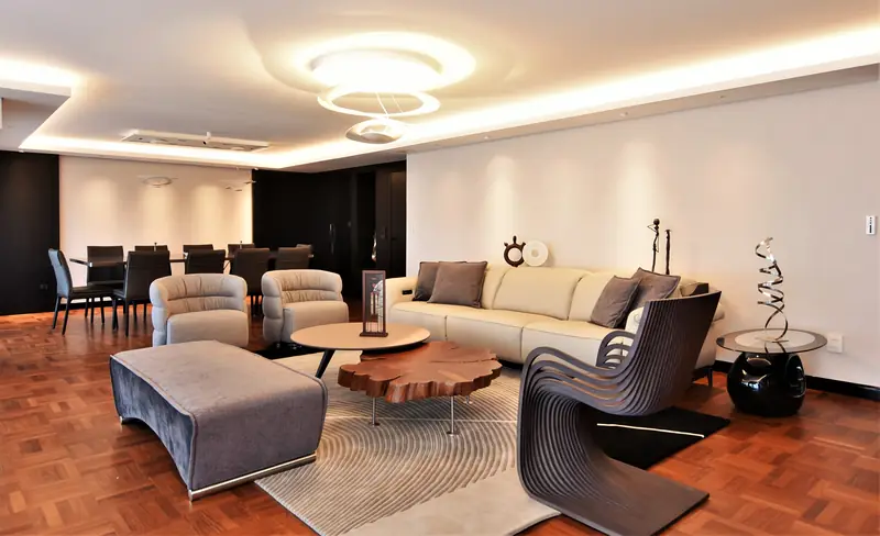 Living con sofá claro, mesa baja de tronco, silla de láminas de madera curvada y lámparas de anillos en el techo con luz indirecta