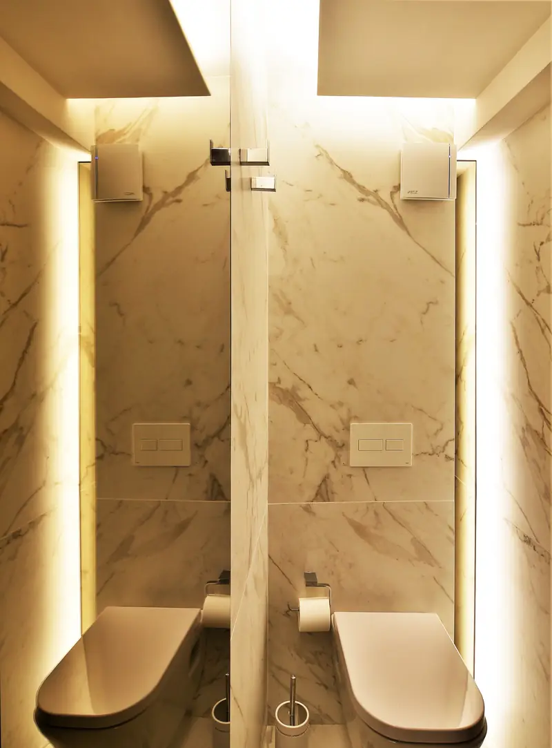 Toilette de mármol veteado con tiras de luz a los lados del espejo