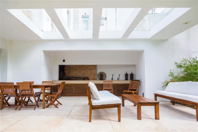 Barbacoa bajo lucernarios con muebles de madera y sillones blancos