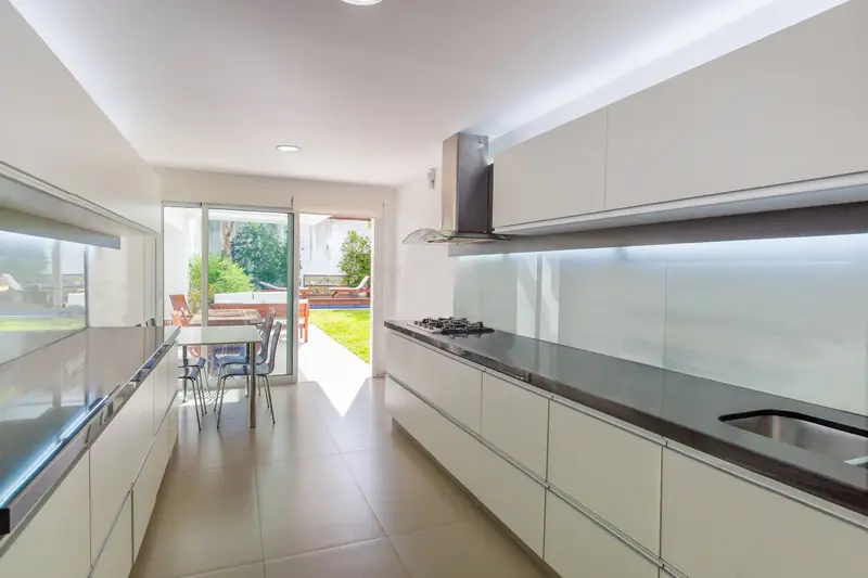 Cocina blanca lineal con mesada oscura que se abre al jardín