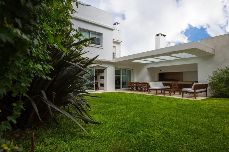 Fachada al jardín con alero blanco y el estar exterior bajo la galería