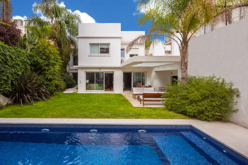 Casa blanca con jardín de césped y piscina de venecitas azules en primer plano