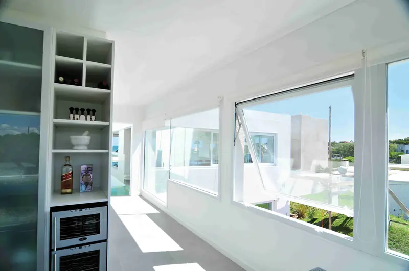 Cocina blanca con estantería abierta y cava de vinos, junto a ventanales corridos con ventanas proyectantes