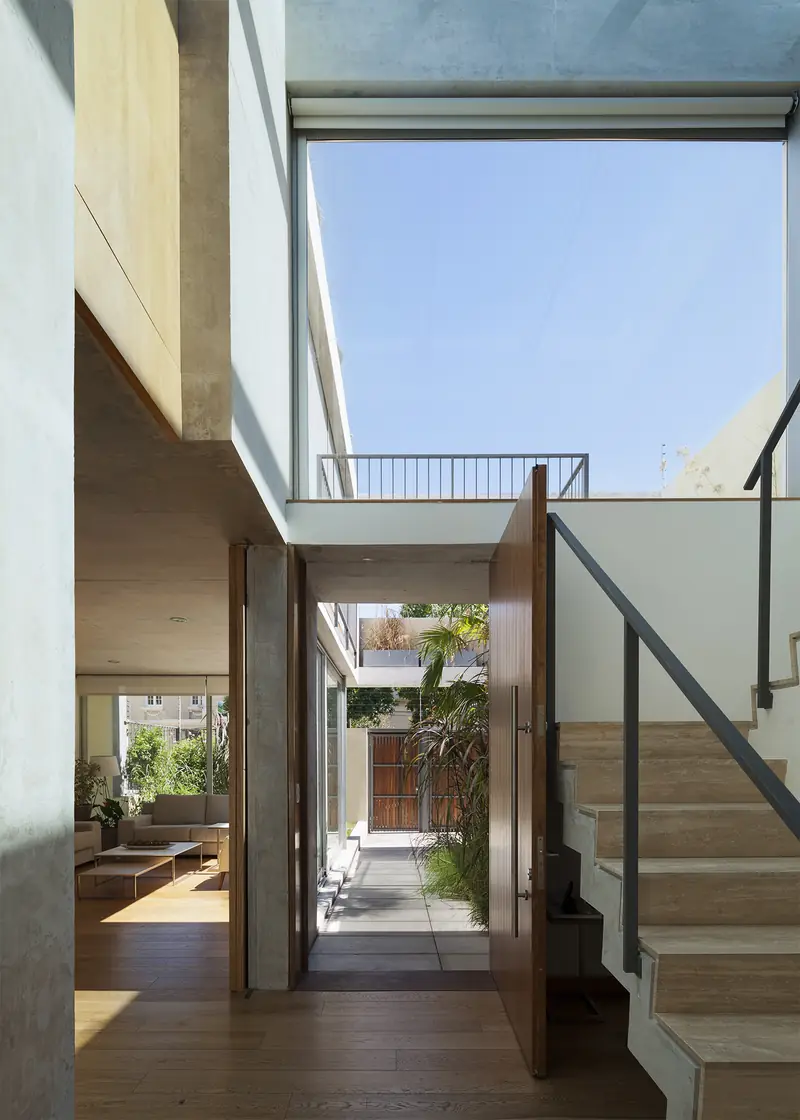 Hall a doble altura con escalera de madera y vidrio y cielo abierto arriba