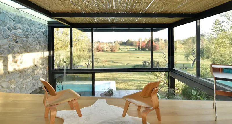 Interior de la caja de cristal bajo el cañizo, con el campo de golf y los árboles al fondo