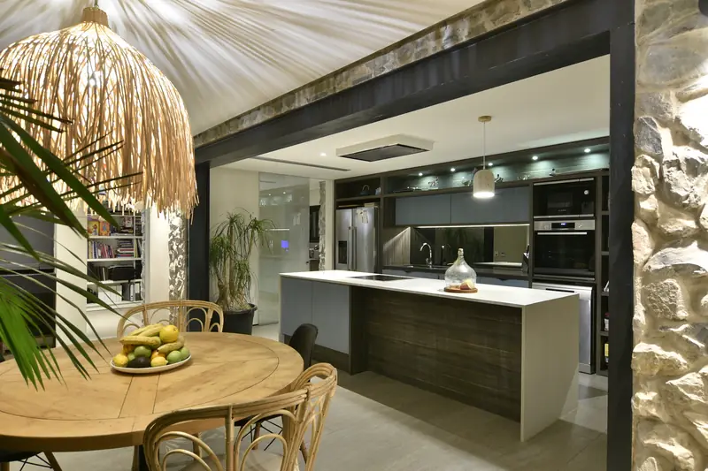 Cocina con isla blanca y mesa redonda de madera junto al muro de piedra