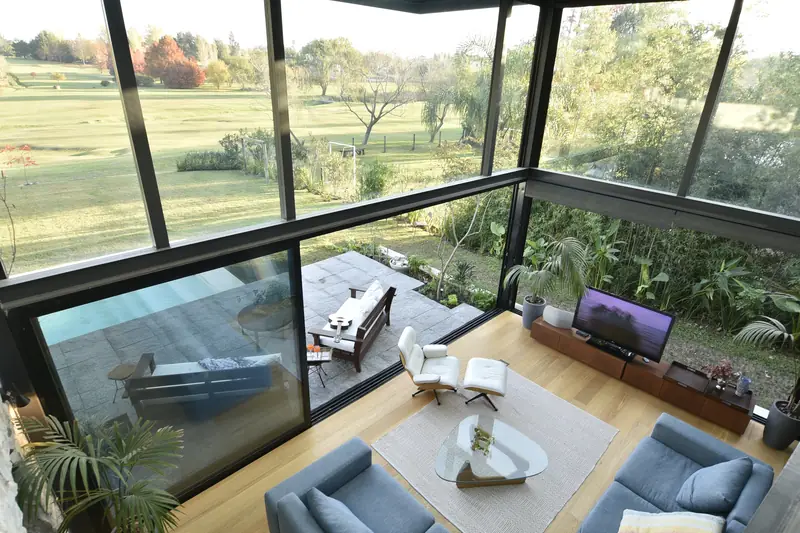 El estar visto desde el entrepiso, con la terraza de piedra y el golf detrás del cristal