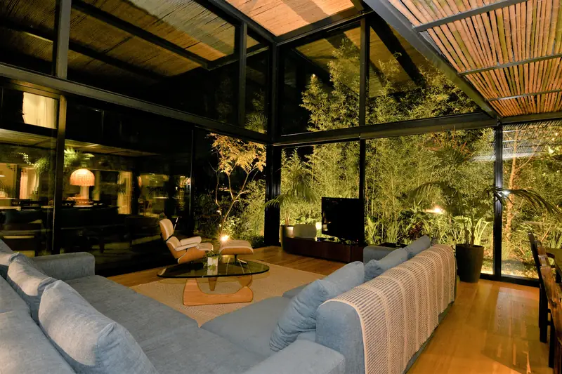 El estar de noche, entre paños de cristal y vegetación iluminada