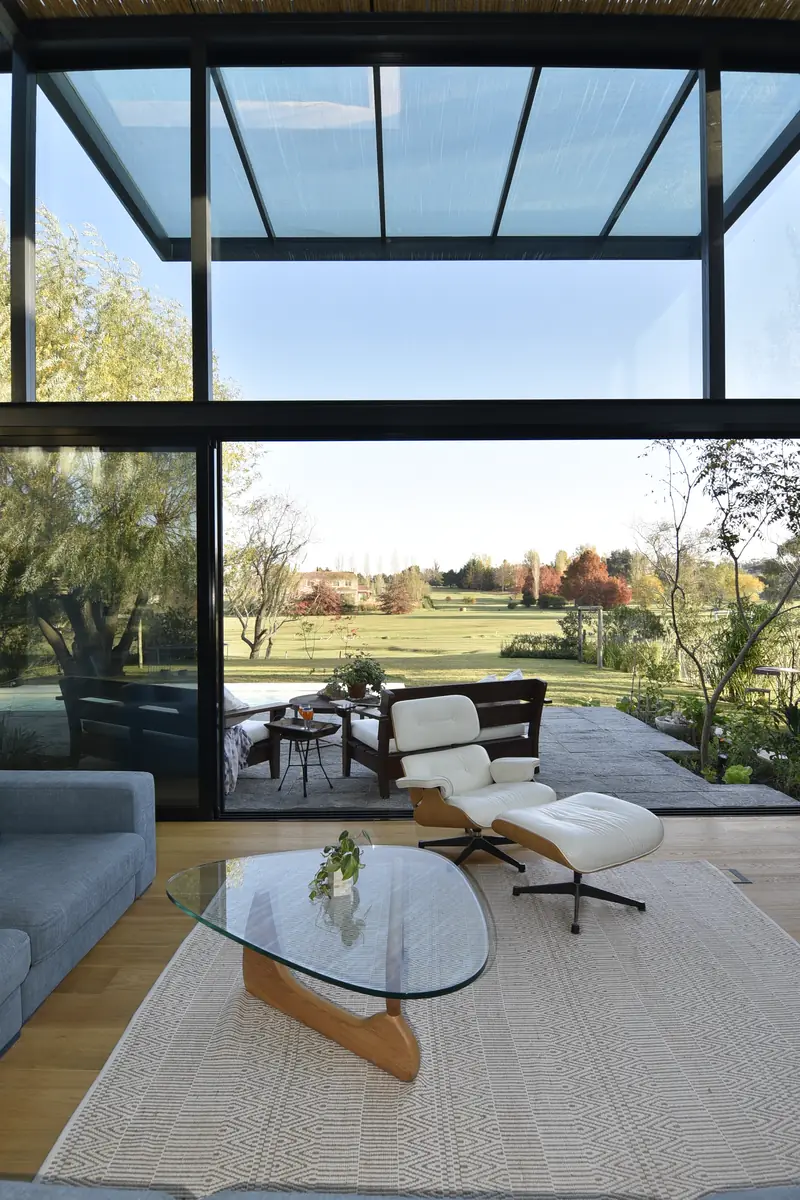 Estar con sillón de cuero y mesa de cristal abierto por completo al campo de golf