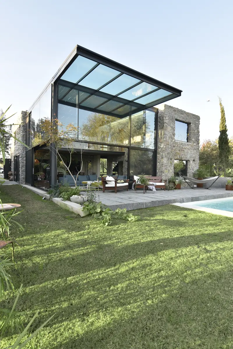 Caja de cristal bajo la pérgola de vidrio junto al volumen de piedra, con la piscina y el césped hacia el golf