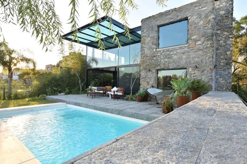 Piscina con borde de piedra junto al volumen de piedra y la caja de cristal con techo de vidrio