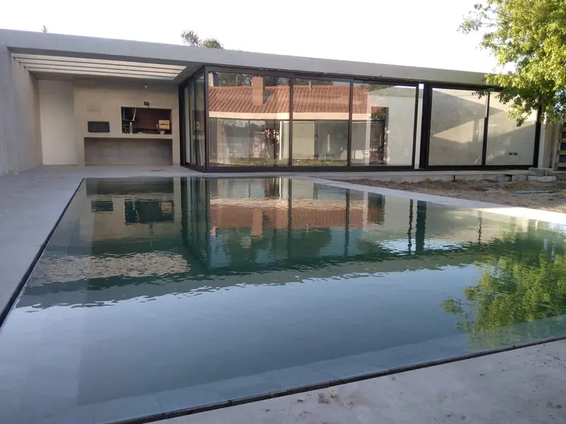 Volumen largo de hormigón y cristal reflejado en la piscina del patio
