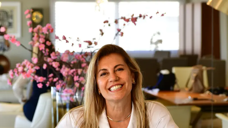 La arquitecta Karin Bia sentada en una sala, sonriendo, con un jarrón de flores de cerezo detrás
