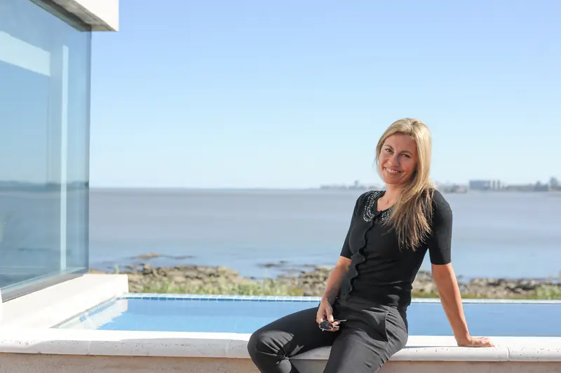 La arquitecta Karin Bia sentada junto a una piscina, con el Río de la Plata detrás