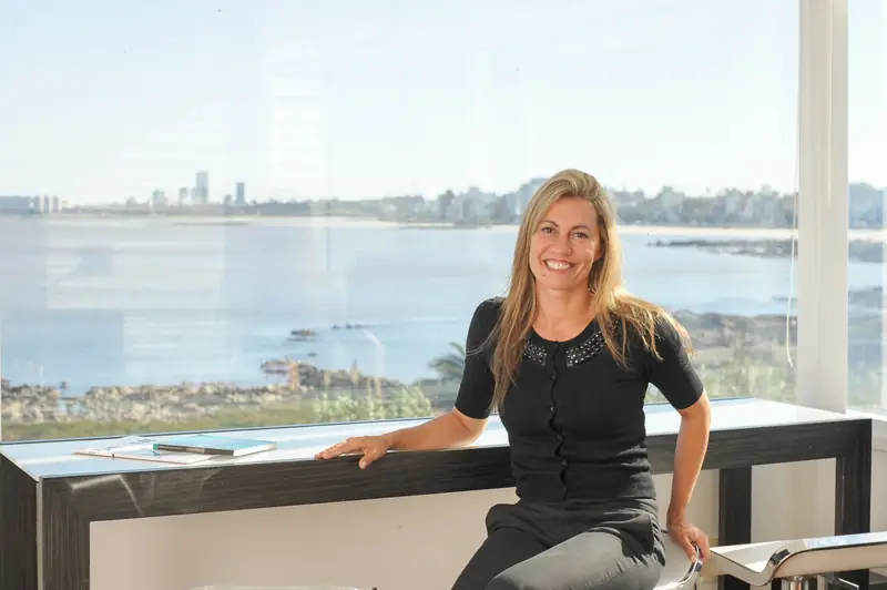 Karin Bia junto a un ventanal con la costa de Montevideo al fondo