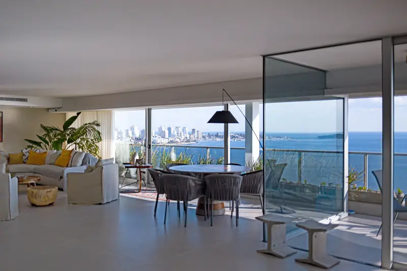 Living del penthouse con la caja de cristal del jardín de invierno y ventanales hacia el agua y la ciudad