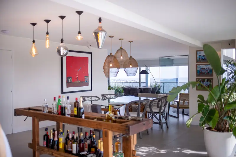 Barra de madera maciza con botellas y lámparas colgantes, con el comedor y los ventanales al fondo