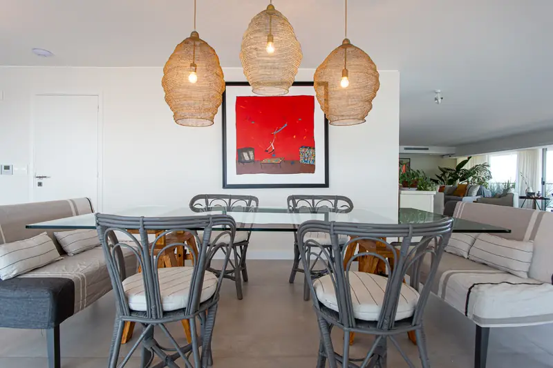 Mesa de comedor de cristal bajo tres lámparas de mimbre y un cuadro rojo