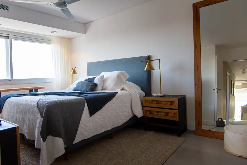 Dormitorio con cabecero azul, ventanal y espejo de pie