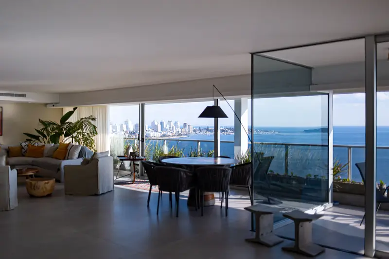 Living del penthouse con la caja de cristal del jardín de invierno y ventanales hacia el agua y la ciudad