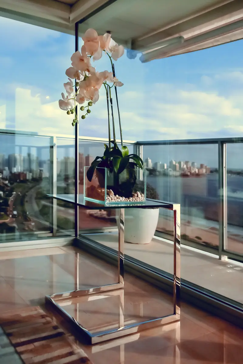 Orquídea blanca sobre una mesa de cristal junto al ventanal del balcón, con el agua al fondo